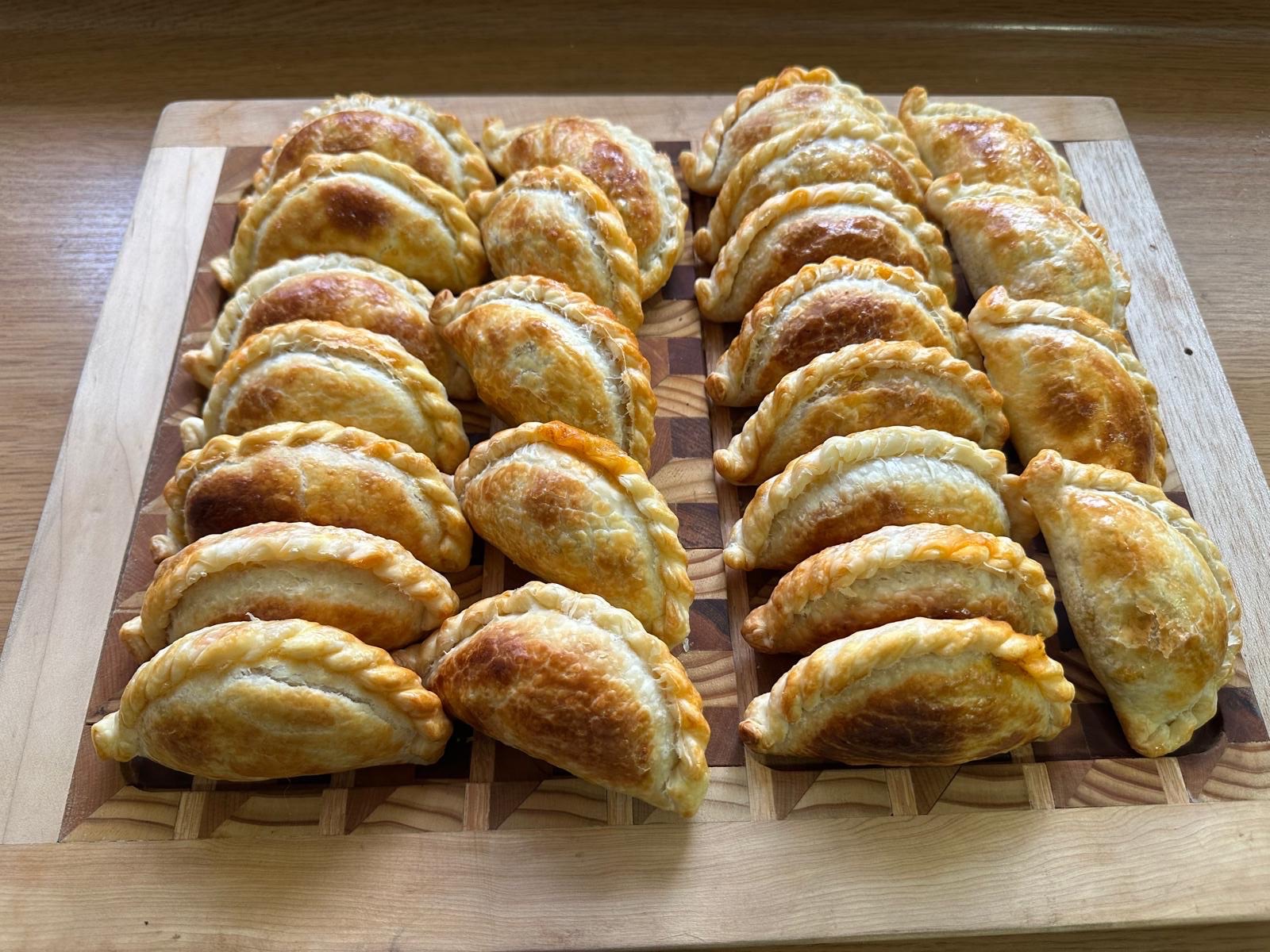 Two dozen empanadas on an end-grain board, seen at an angle