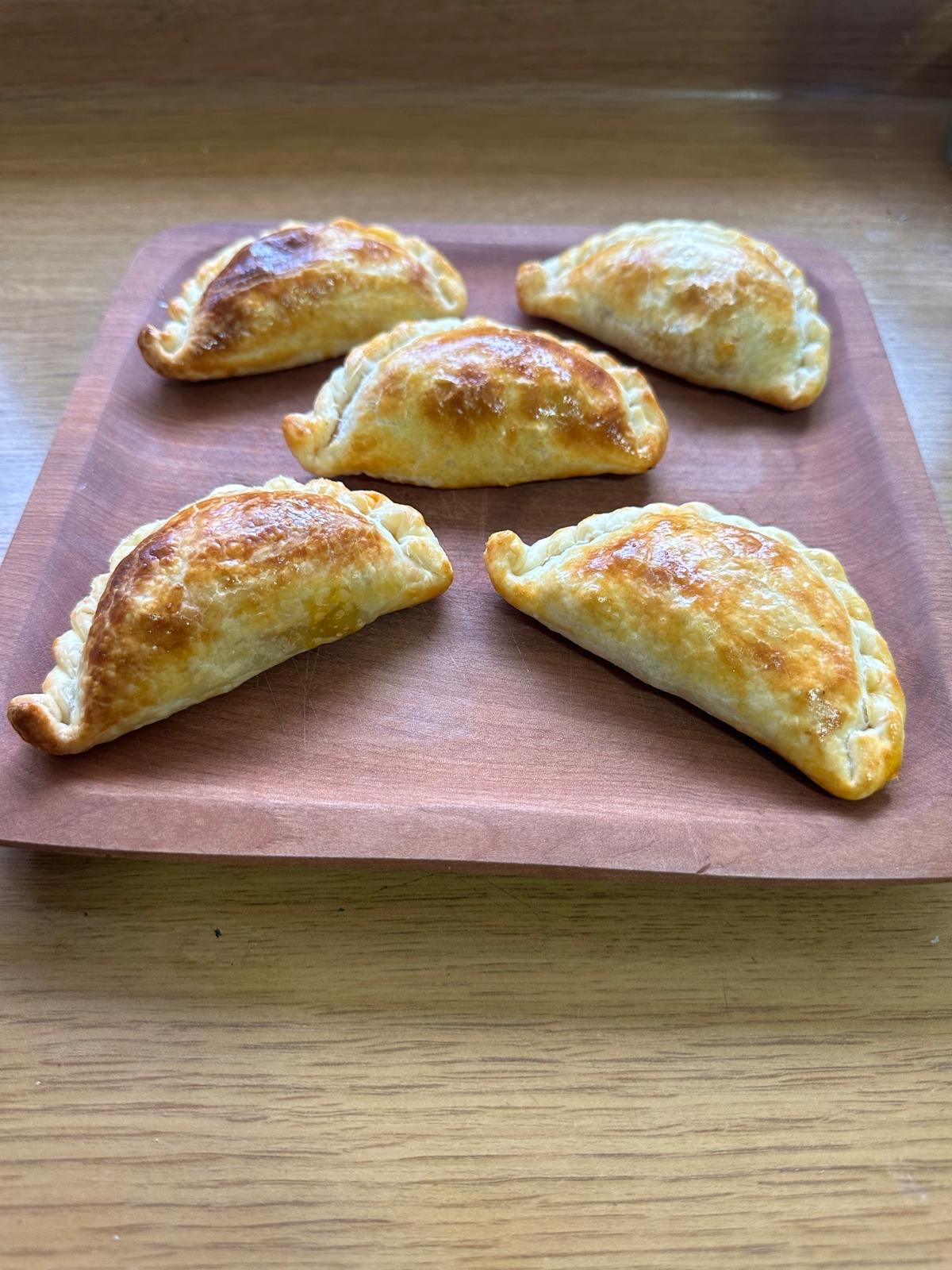Five baked empanadas on a wooden tray