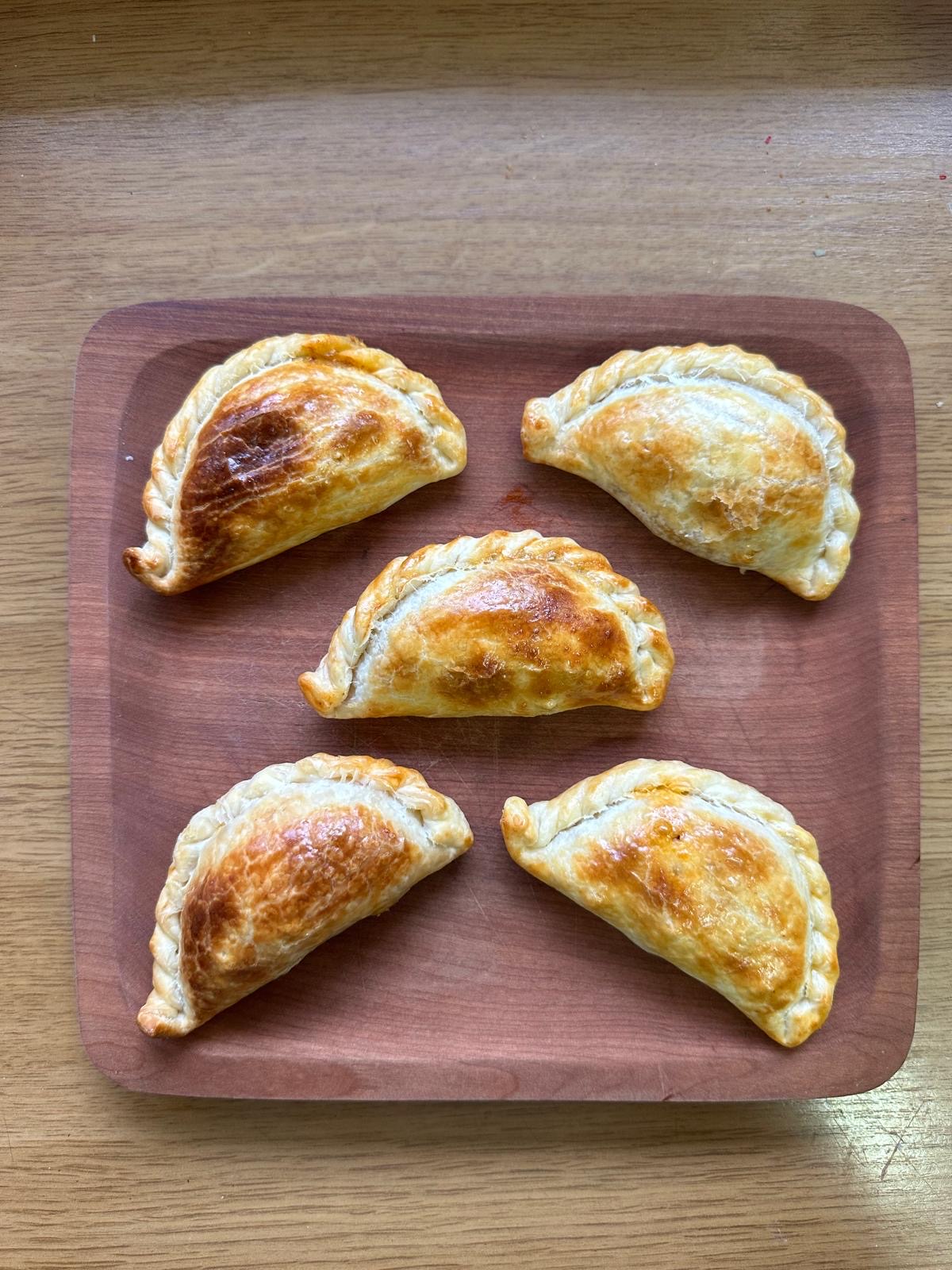 Five empanadas on a red wooden tray, seen from above